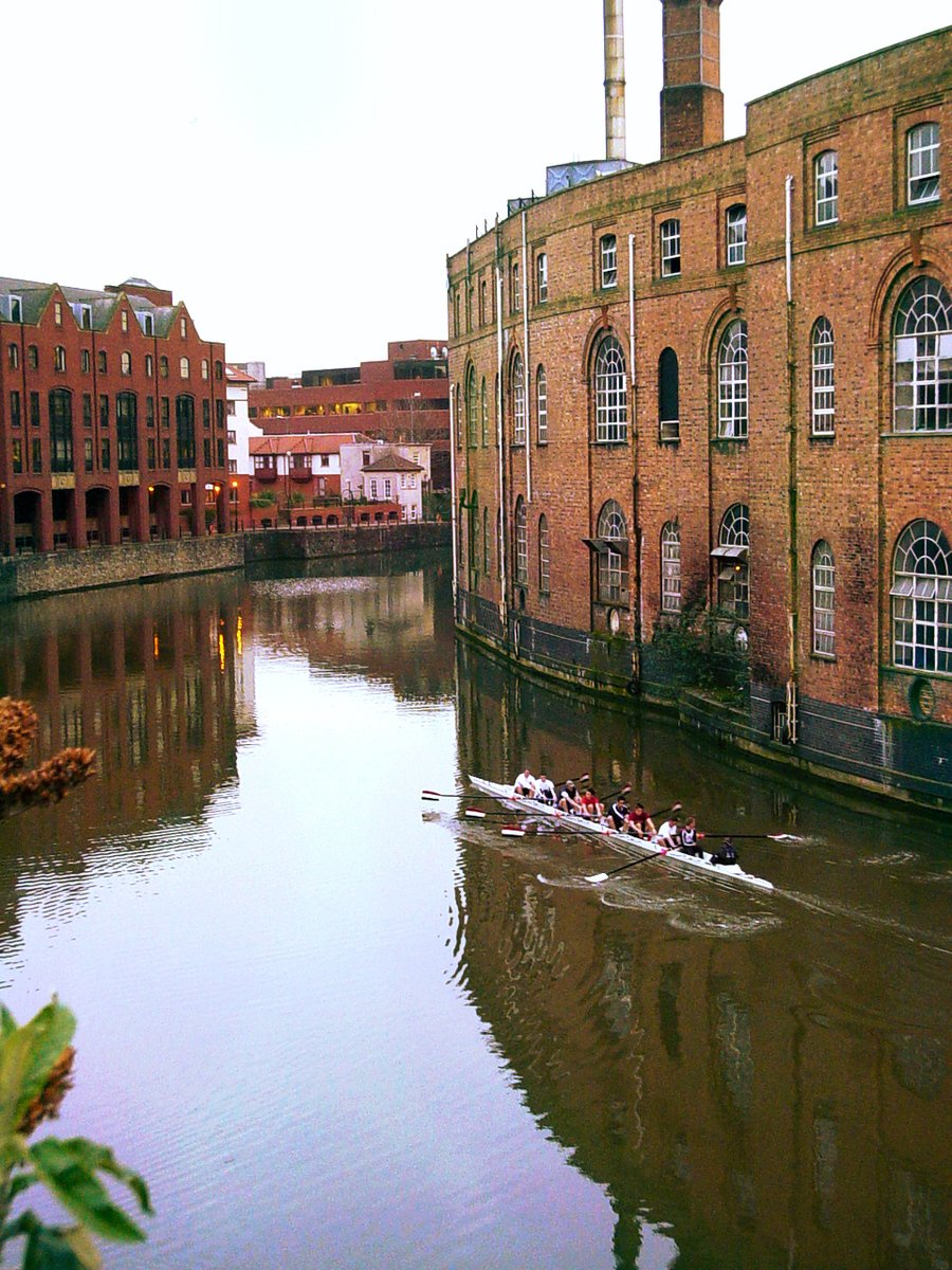 there are rowers rowing down the river by brick buildings