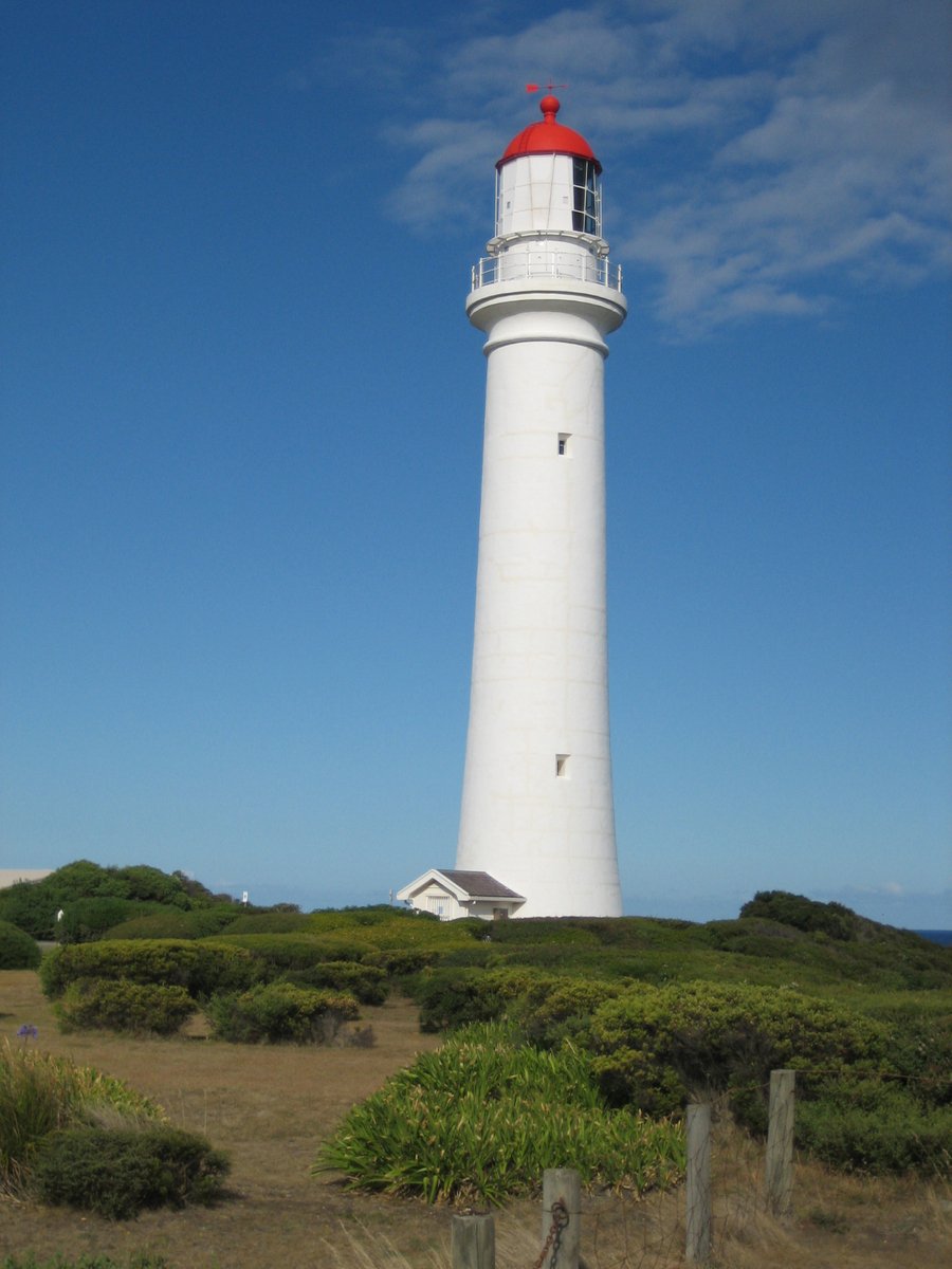a white lighthouse stands in front of a grassy hill