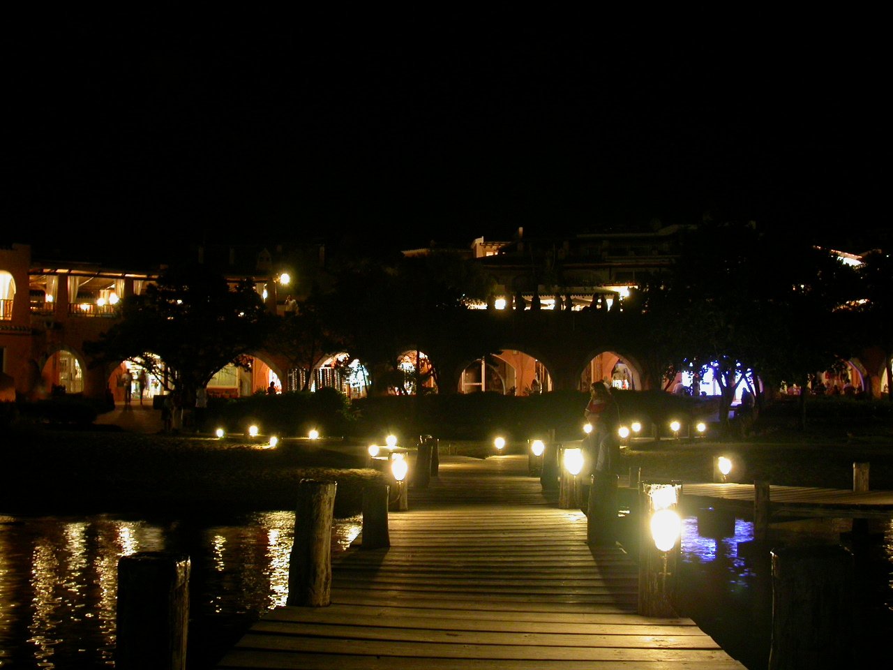 a lit walkway by a body of water with some lights