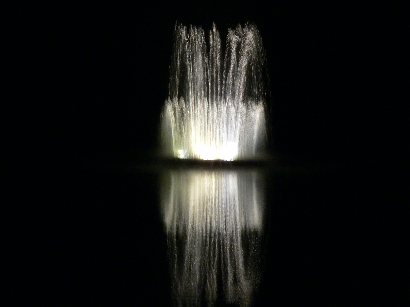 fireworks are glowing from the dark behind a fountain