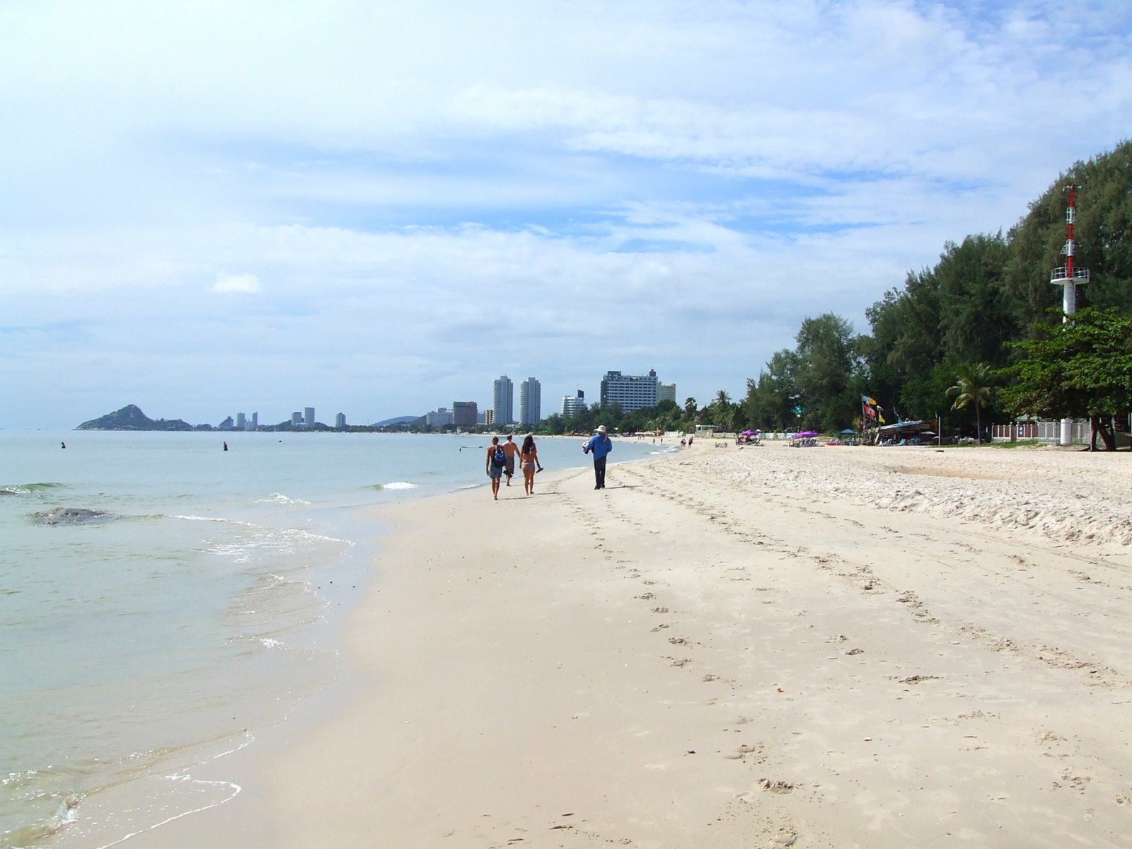 three people are walking on the beach near some water