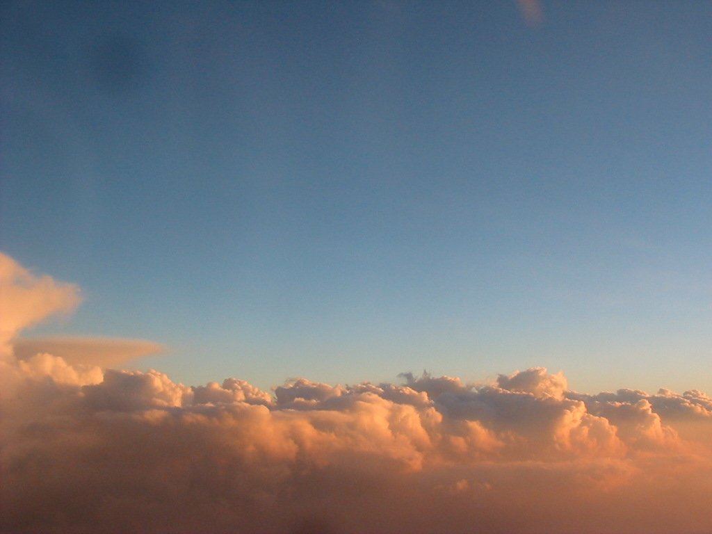 a plane flies in the clouds on a sunny day