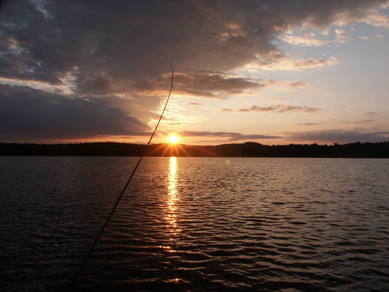 the sun is setting over a lake and there is a fishing pole