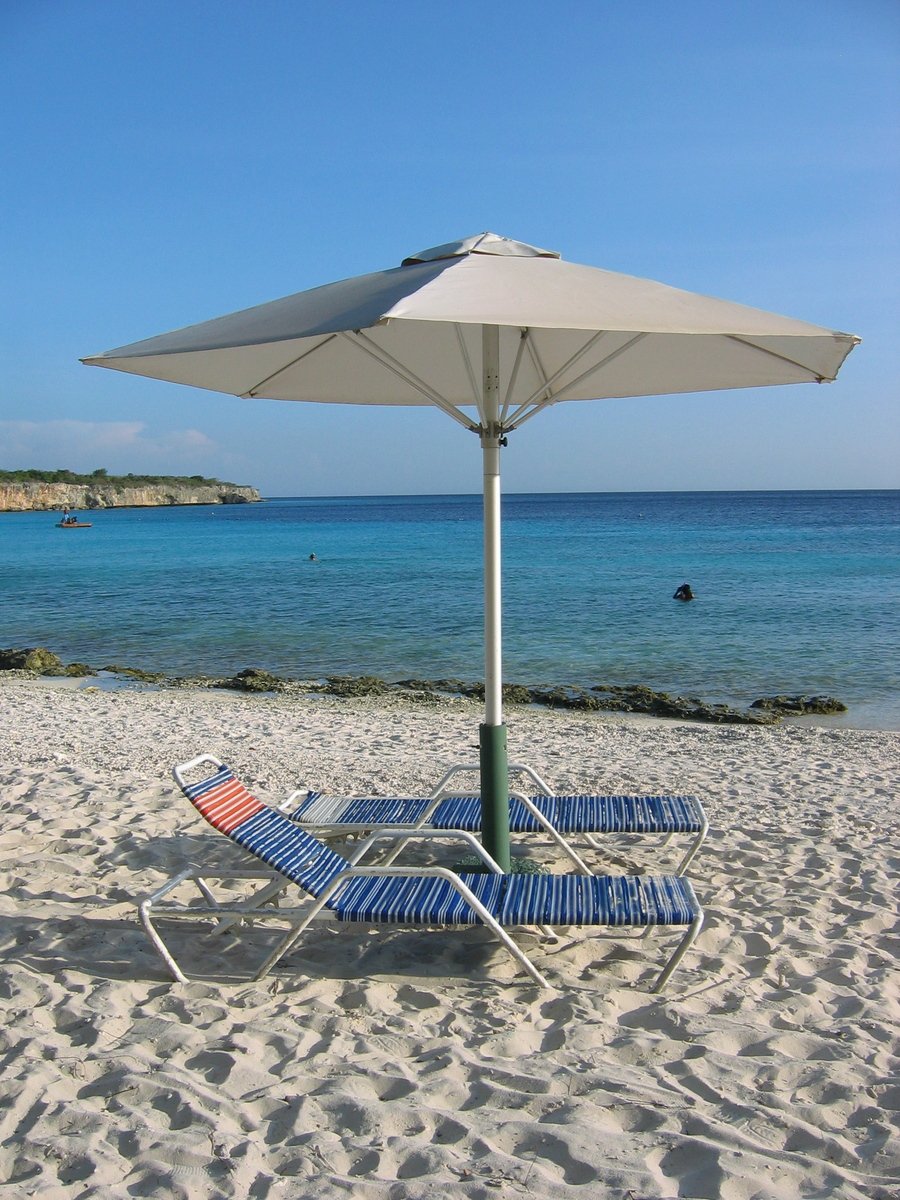 two lawn chairs on the beach under an umbrella