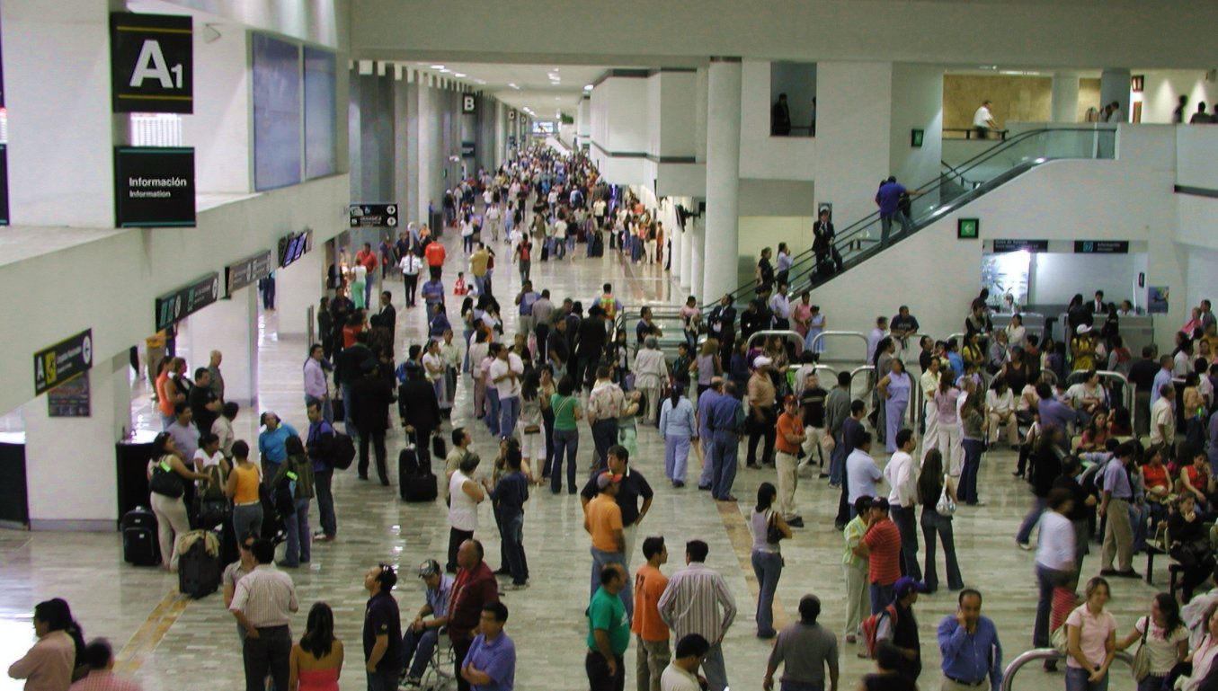 a busy crowd of people walk inside an airport