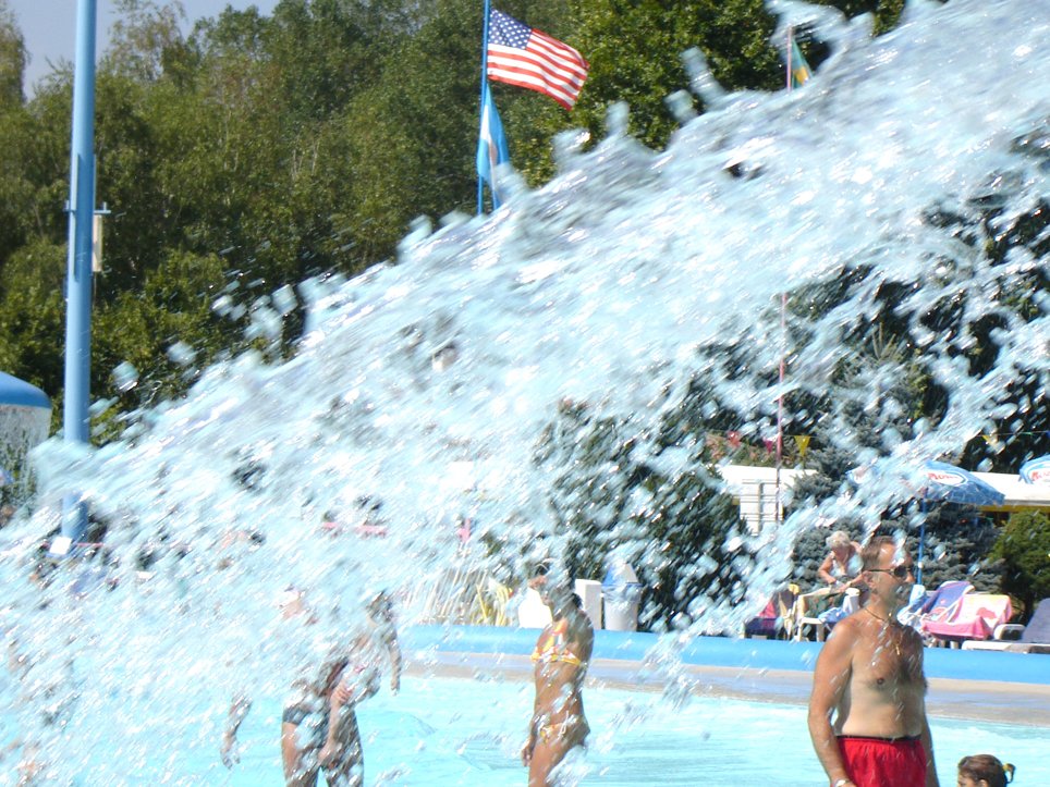 a man standing near a blue swimming pool with a bunch of people playing in it