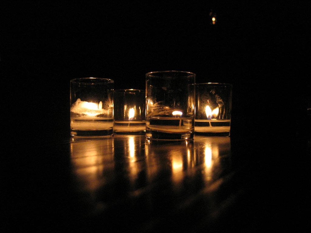 candles are lit in glasses with some reflection on a table
