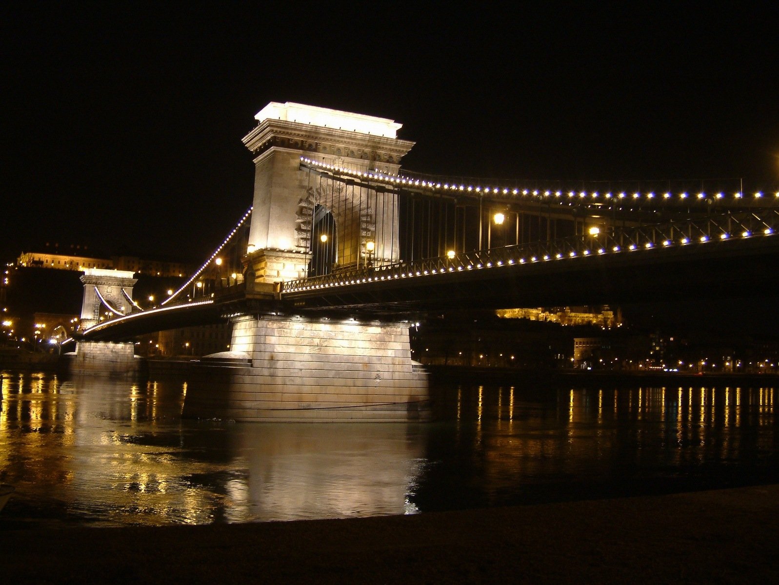 view of a river and bridge at night with lights in the water