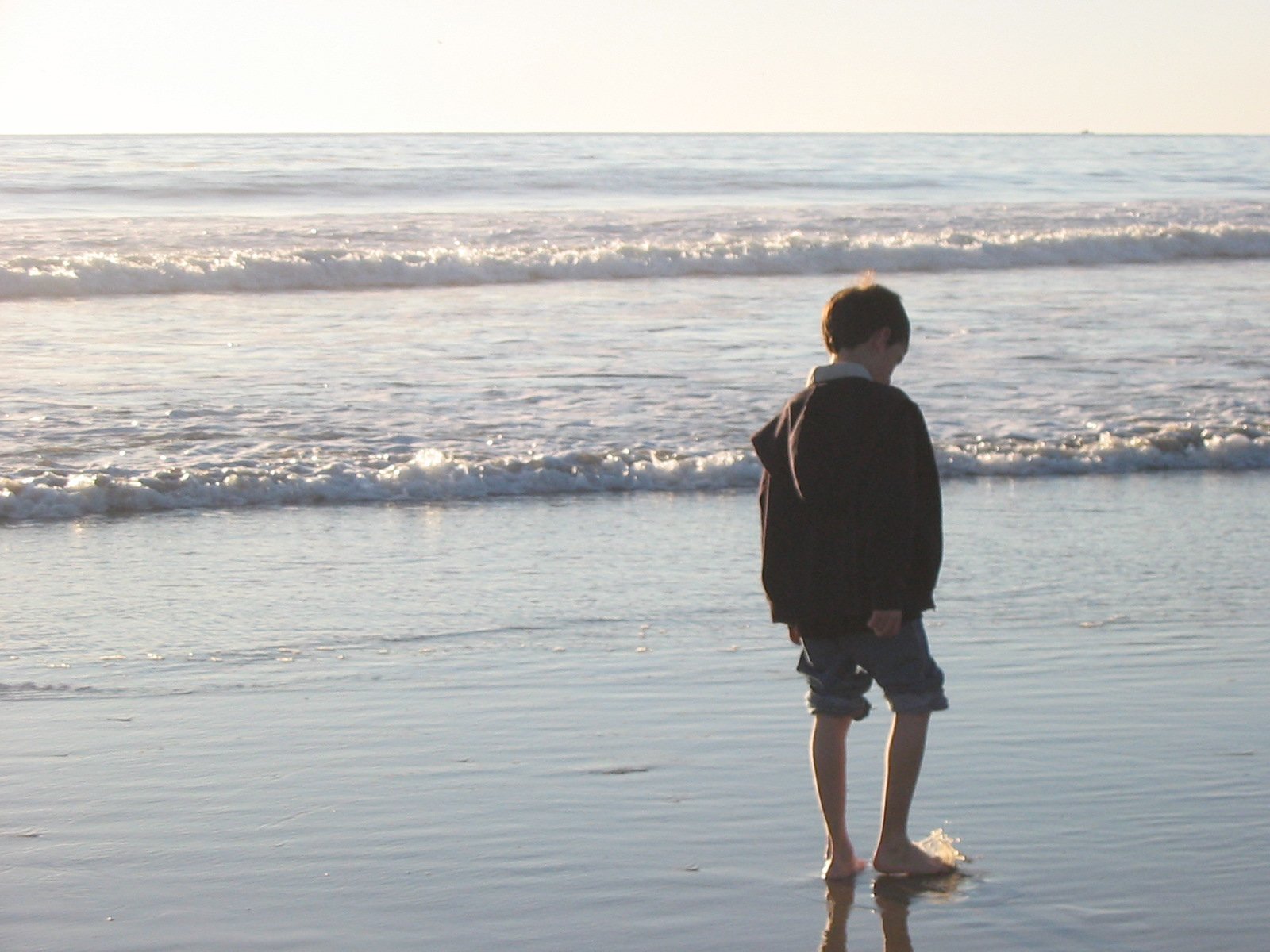 young man walking along the beach with a clear ocean in the background