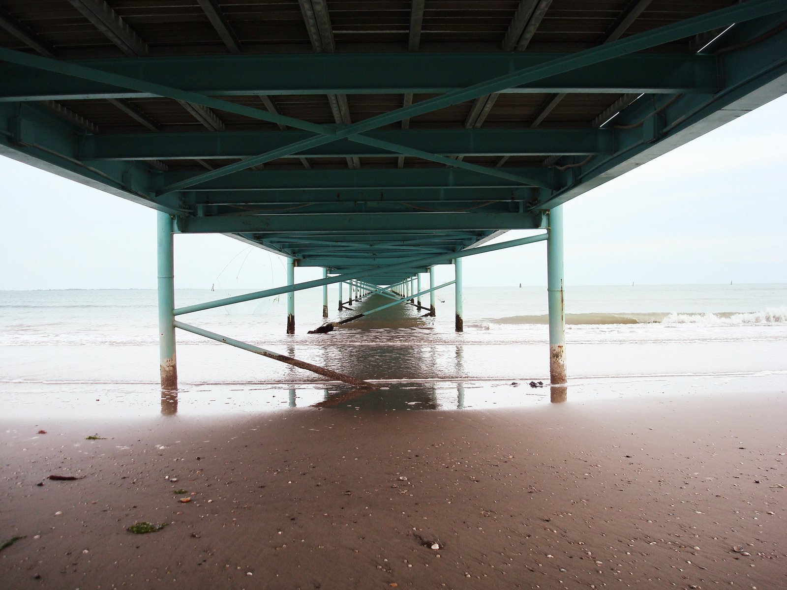 the underside of an empty pier on a beach