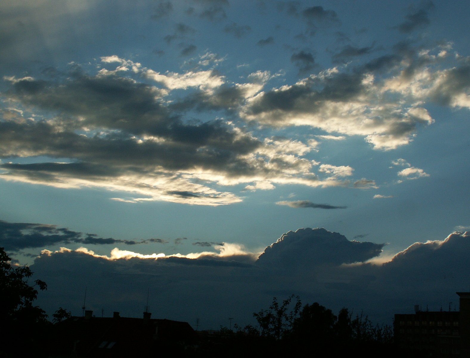 a large cloud is silhouetted against the dark blue sky