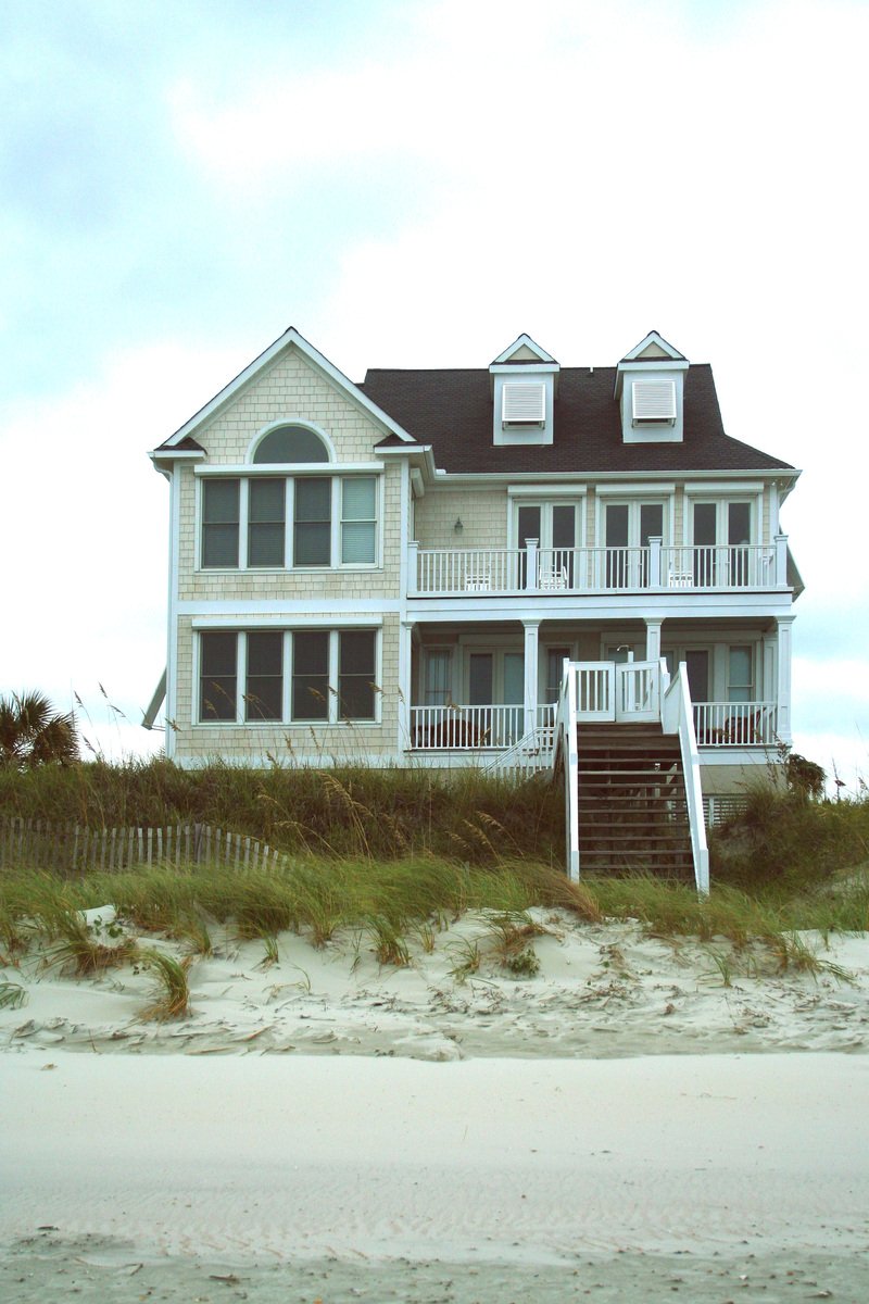 two large beach homes on the side of a sandy beach