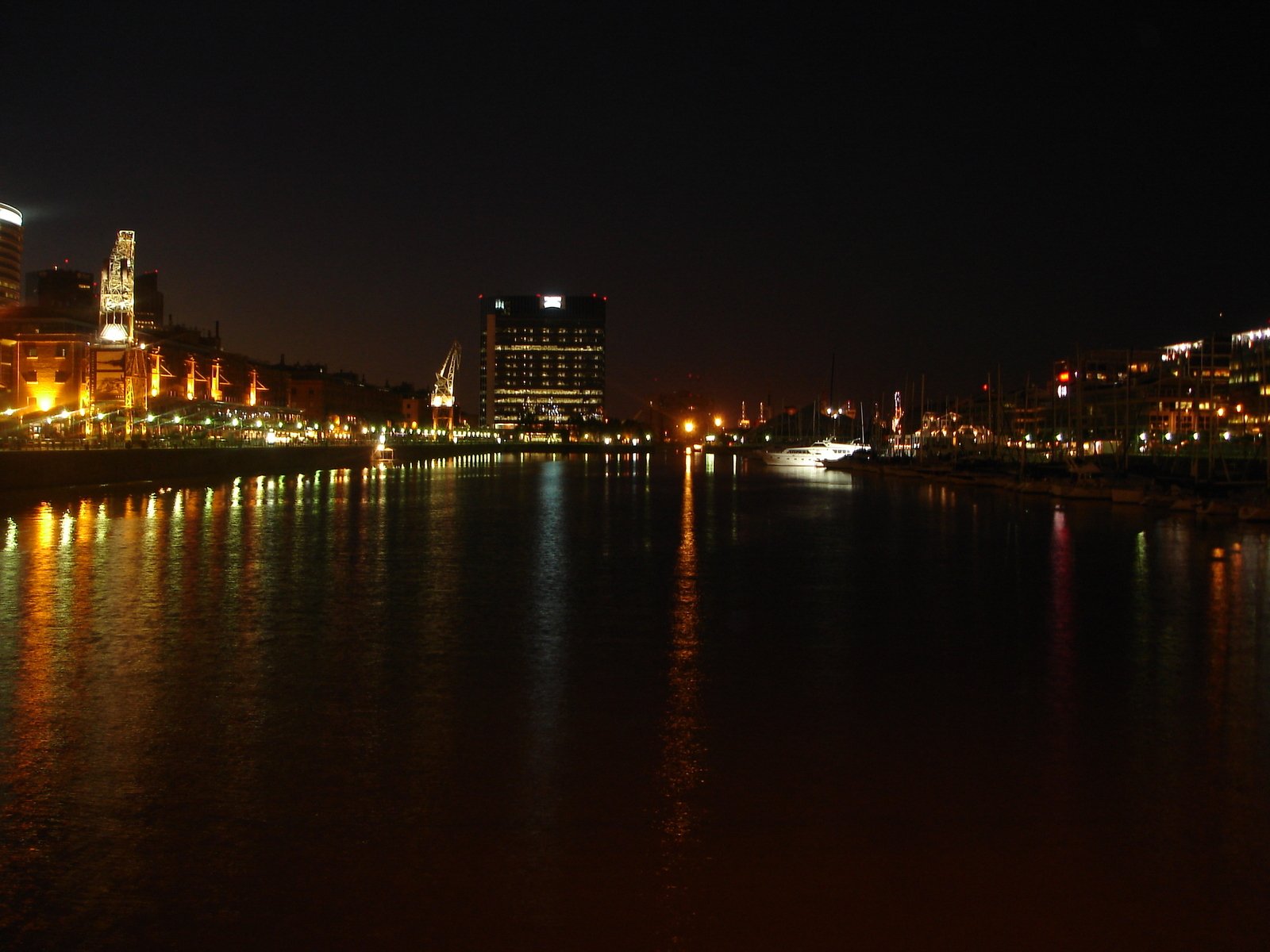 a nighttime s of some buildings with lights and a lake in the foreground