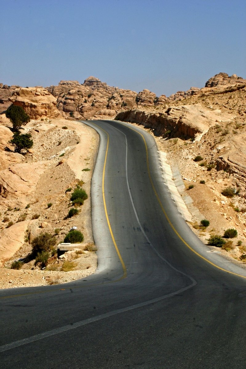 an empty road leading through the desert to the distant mountain