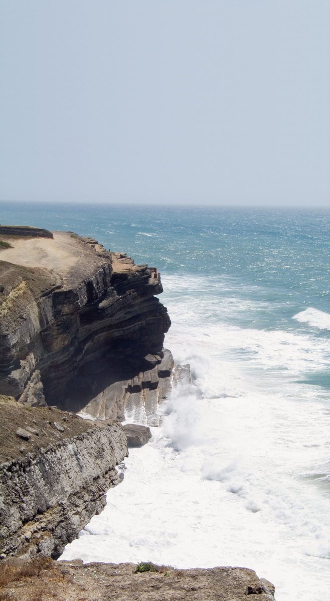 two people are walking down the rocky cliff overlooking the ocean