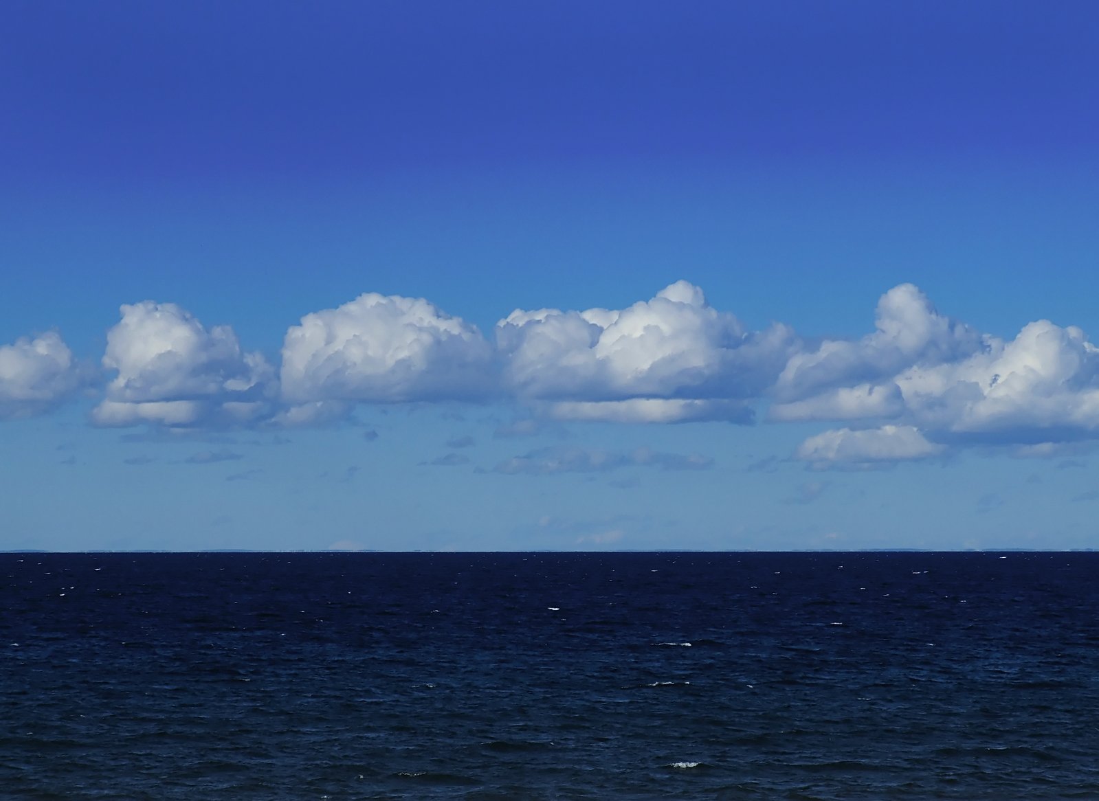 several white clouds float in the blue ocean
