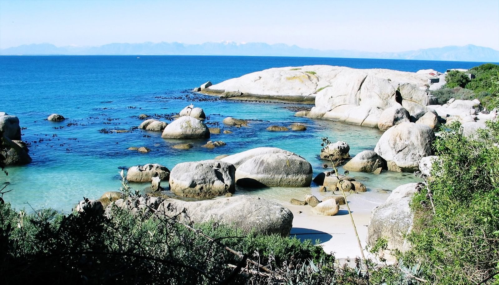 several rocks sit near a small beach and water