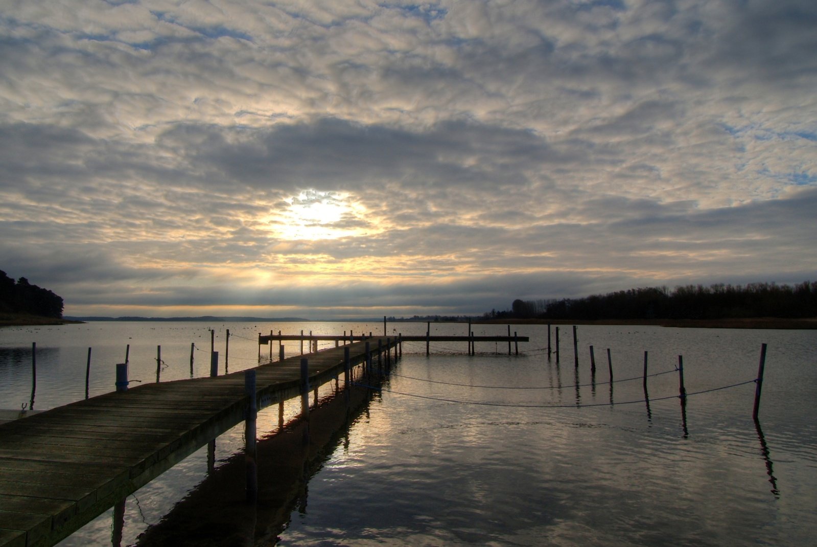 a wooden dock sitting in a lake under a cloudy sky