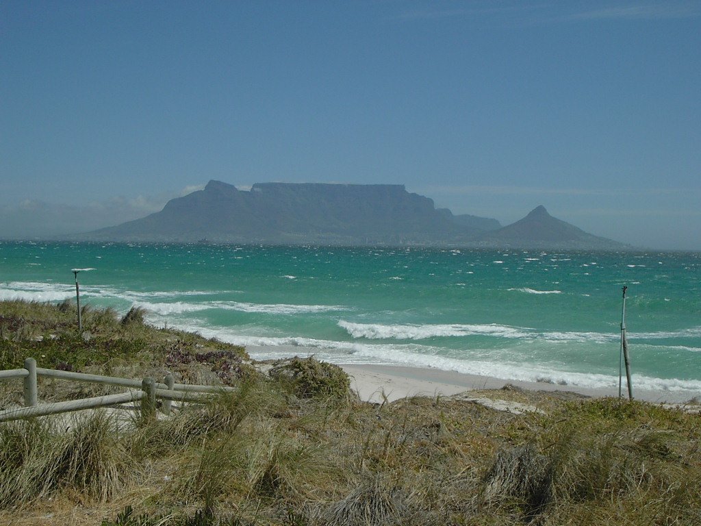 view of beach from the shore of a small beach with some ocean, mountains and a fence