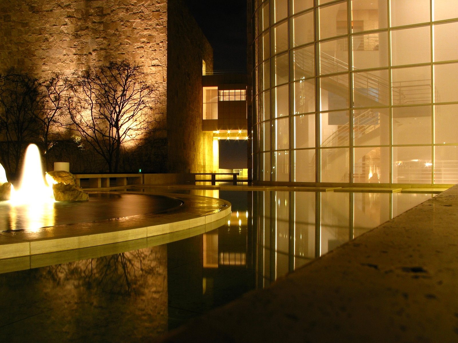 a lighted building in front of a large glass window next to water