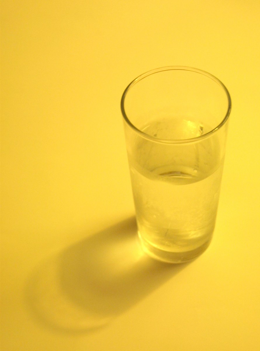 a s glass with some water is on a yellow surface