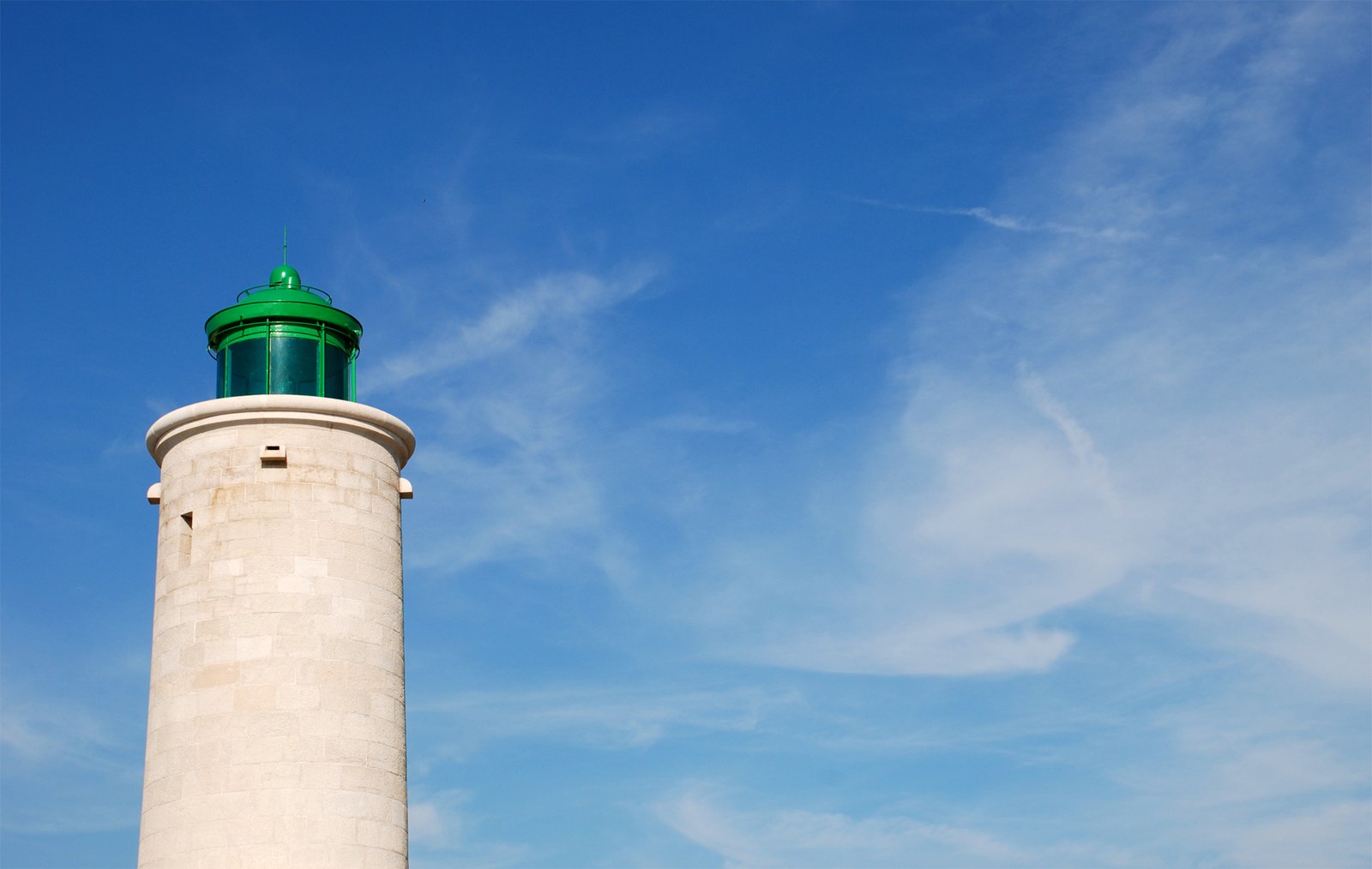 the tall light house is surrounded by a cloud filled sky