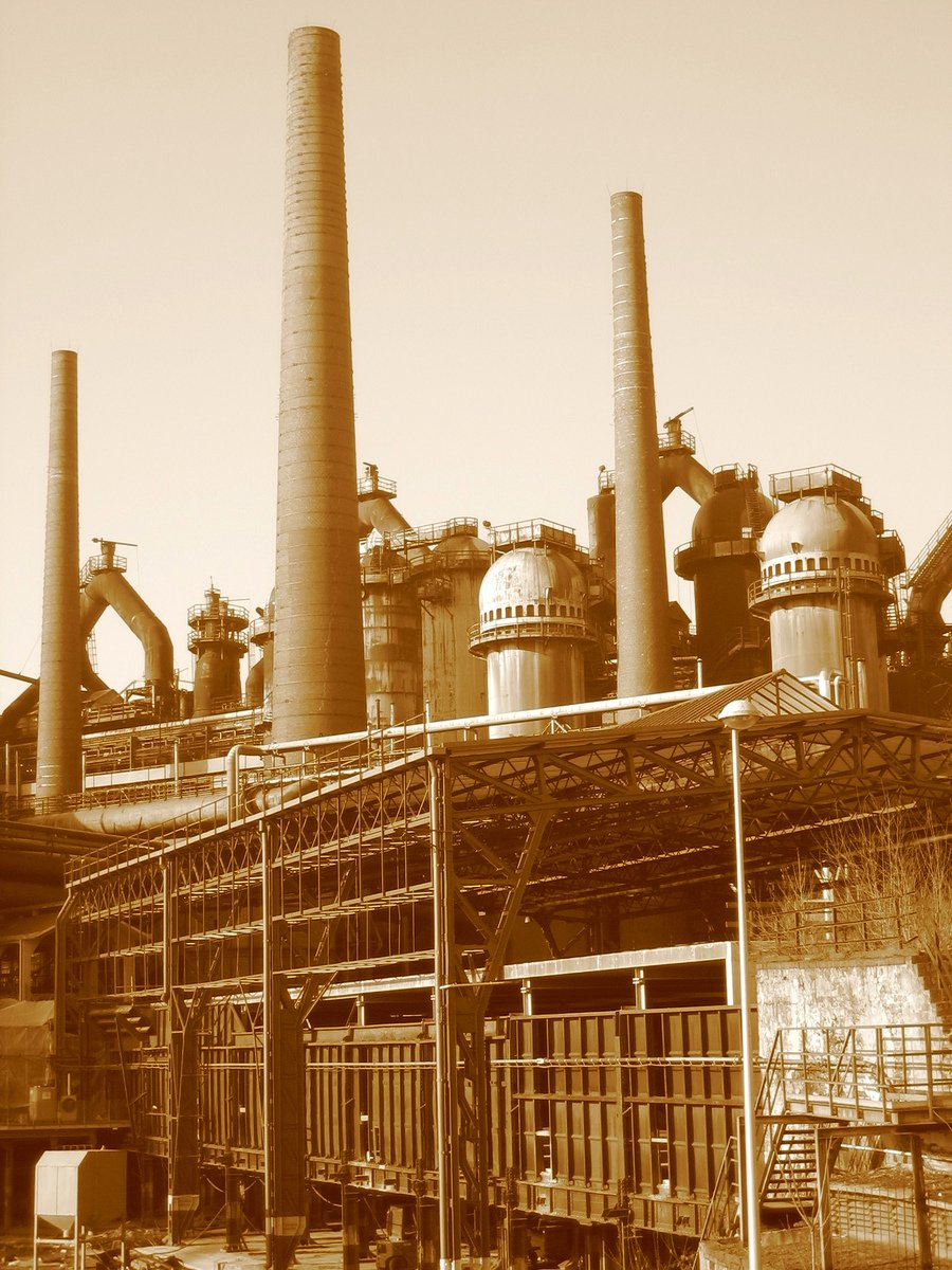 a sepia pograph of an industrial facility with stacks of exhaust pipe