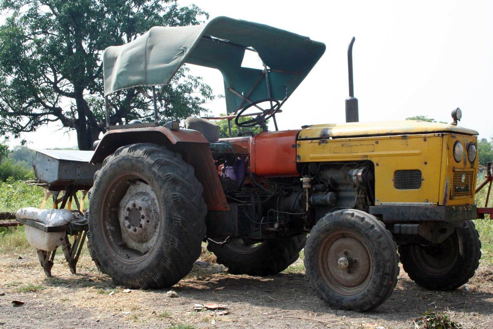 a large tractor sitting in a dirt field next to a tree