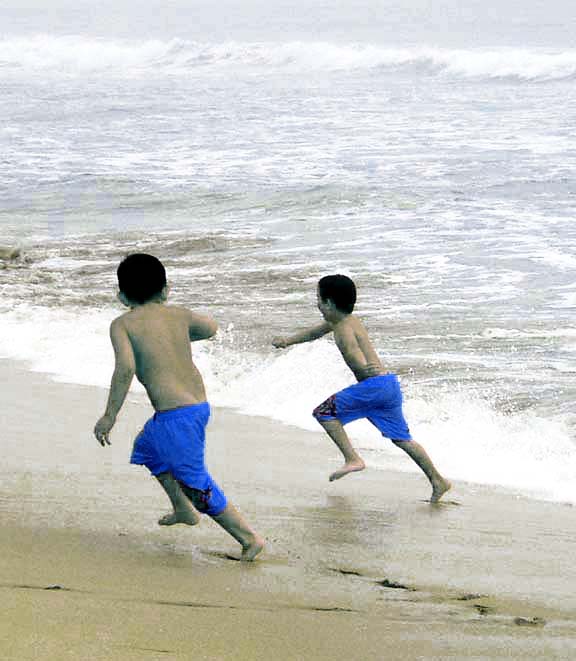 two boys running at the water's edge on a beach