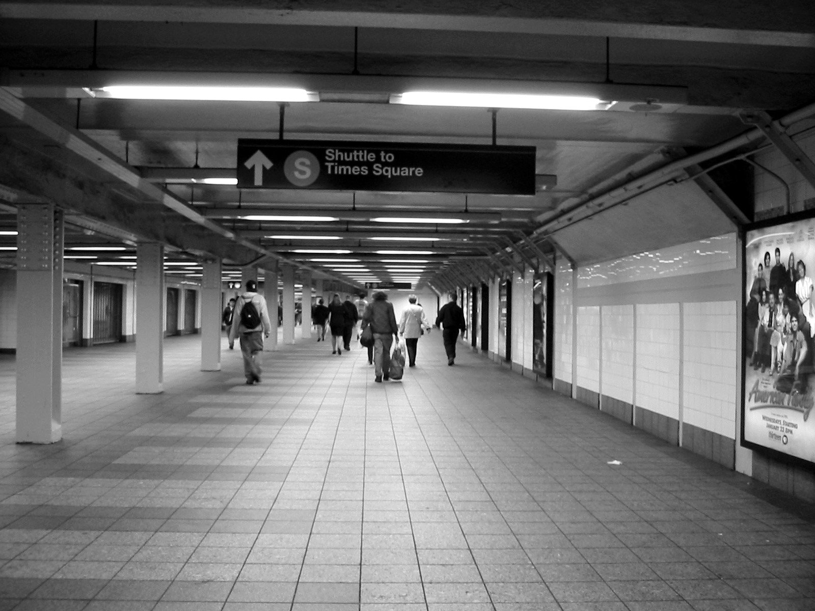 black and white image of people walking along a subway station