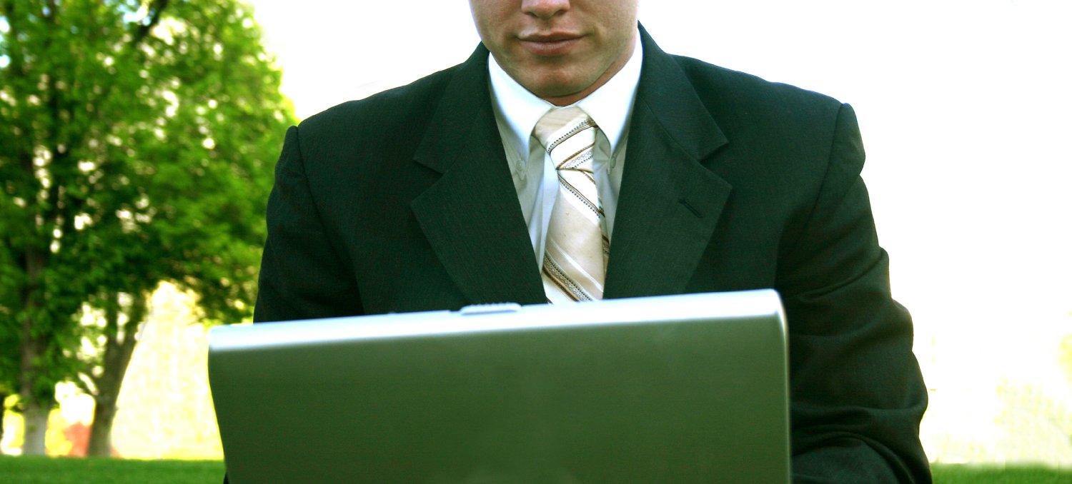 a man in a suit using his laptop on the grass