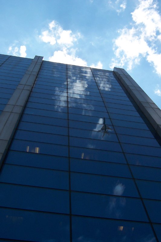 the reflection of the building across the street is of clouds and blue skies