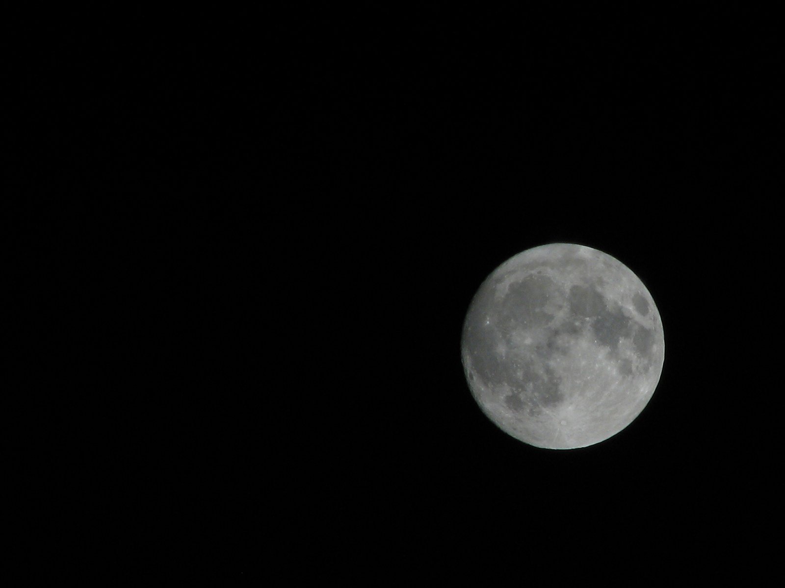 the moon shines in the dark sky, almost obscured by an airplane