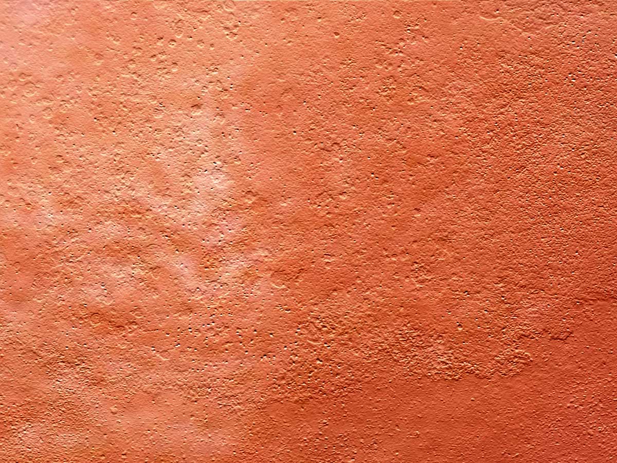 the red stucco wall with rough surface looks like it has been peeling