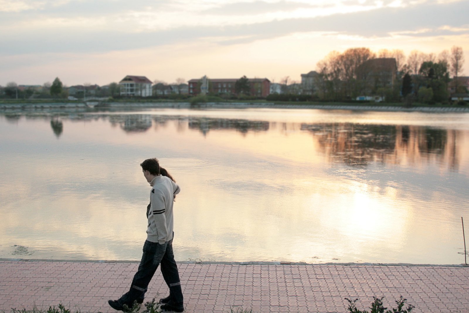 a man walks near a large pond in the evening