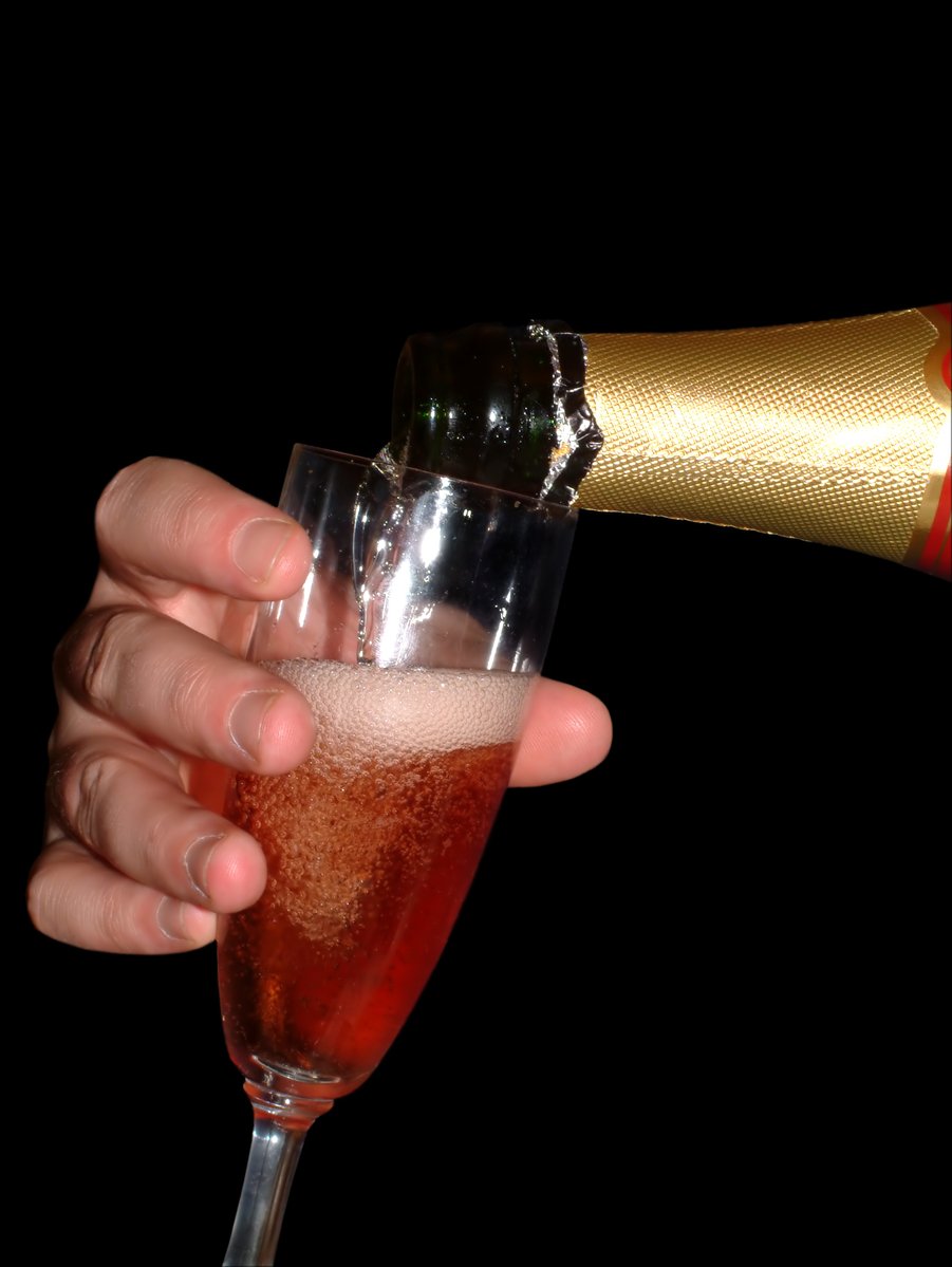 a hand holding a wine glass with red wine in it and a champagne bottle pouring out the top