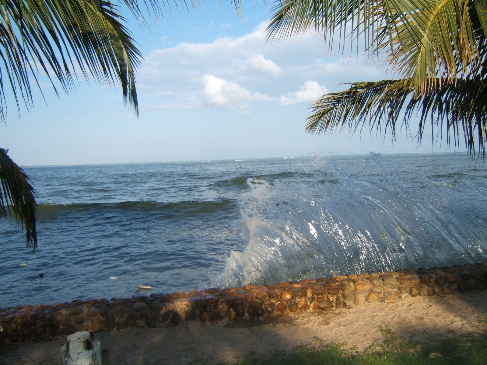 a wave crashes on the beach next to a stone wall