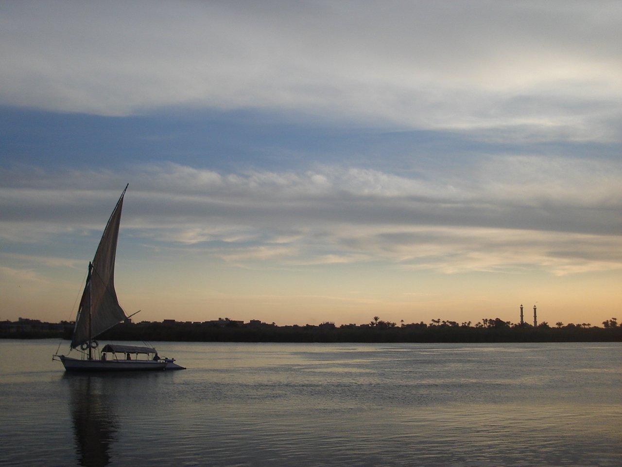 a sailboat sails across a lake as the sun sets