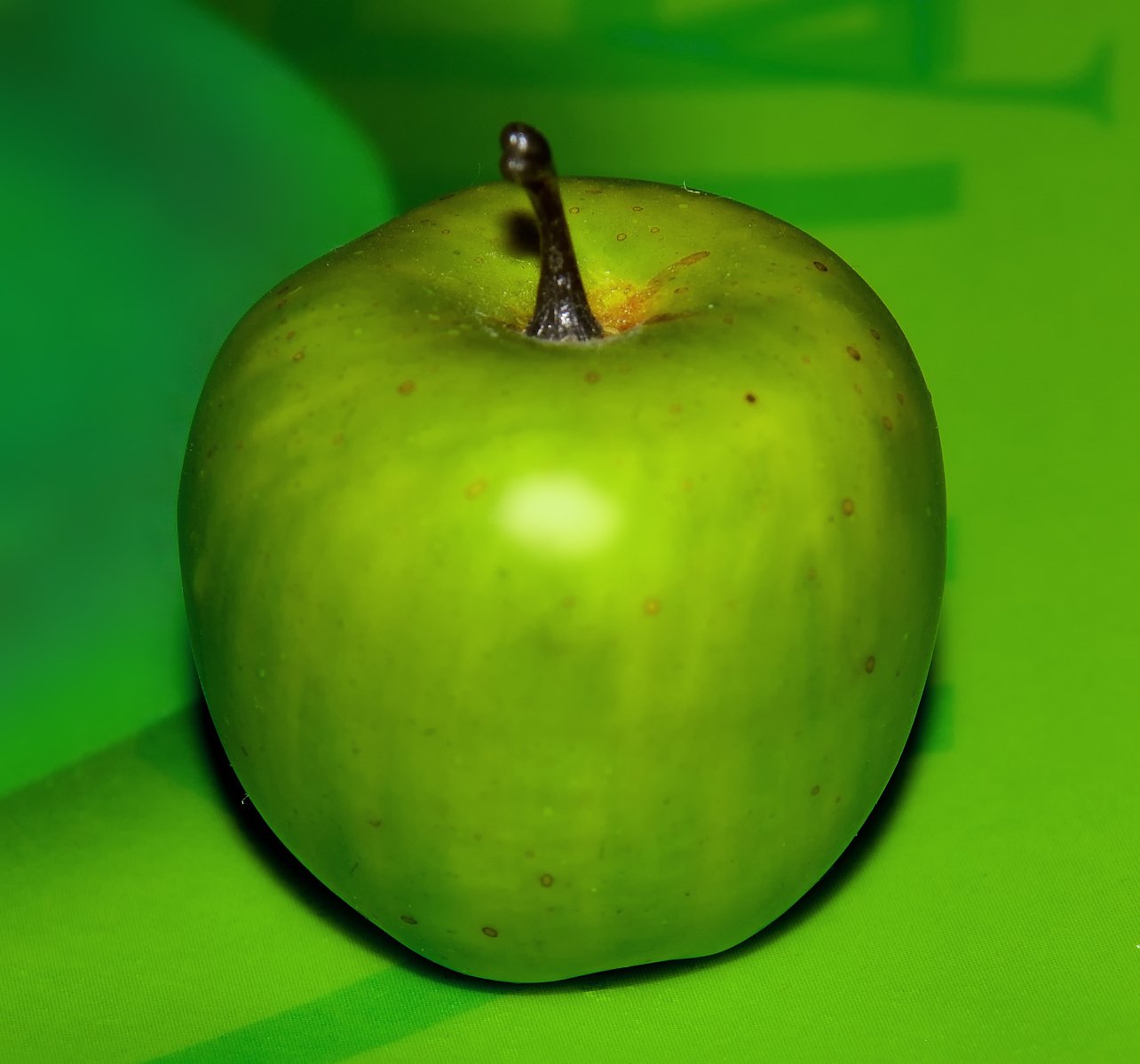 an apple with a black stem sitting on a green surface