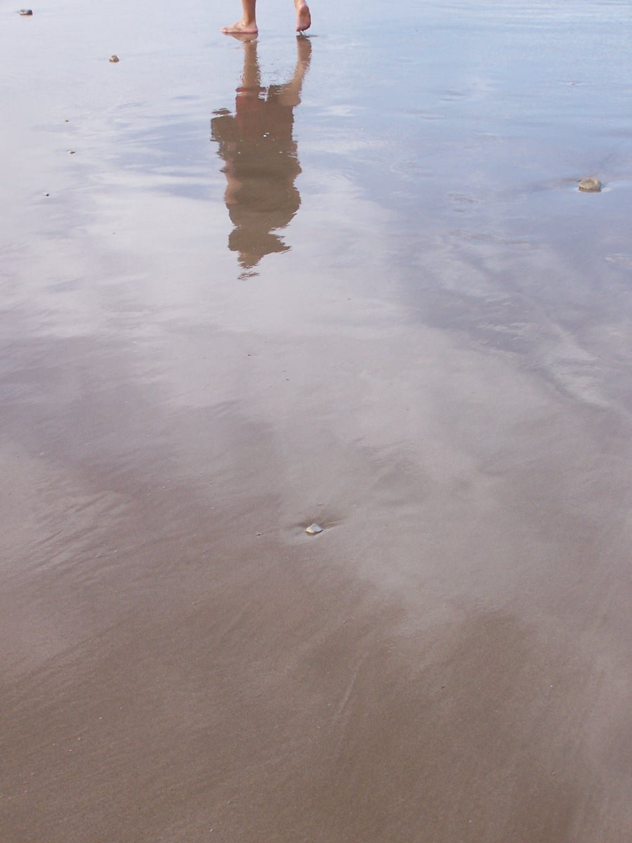 a person in white top standing on a beach by the ocean