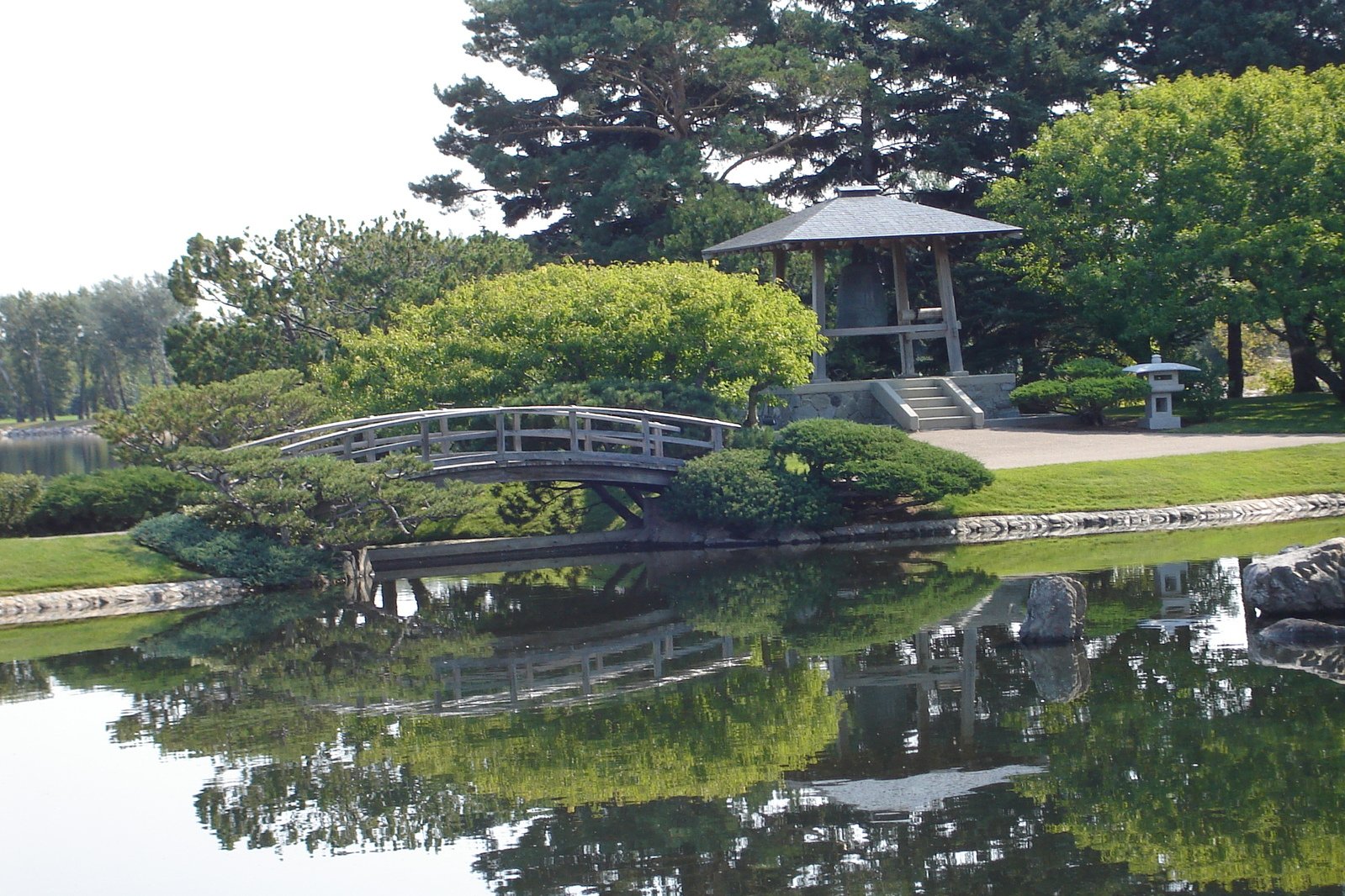 a view of a park in the day, including a bridge and water pond