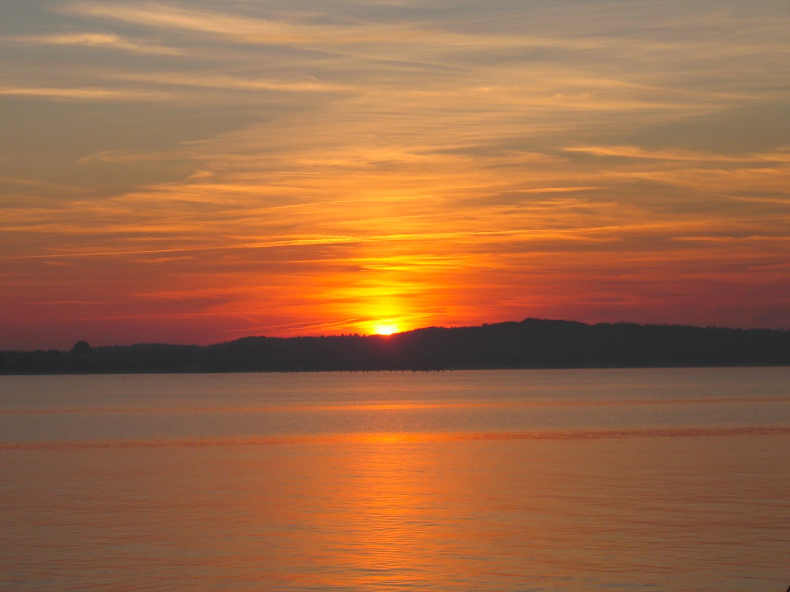 a sunset seen over water with hills in the background