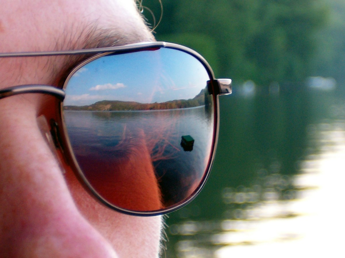 a reflection of a man in his sunglasses near the water