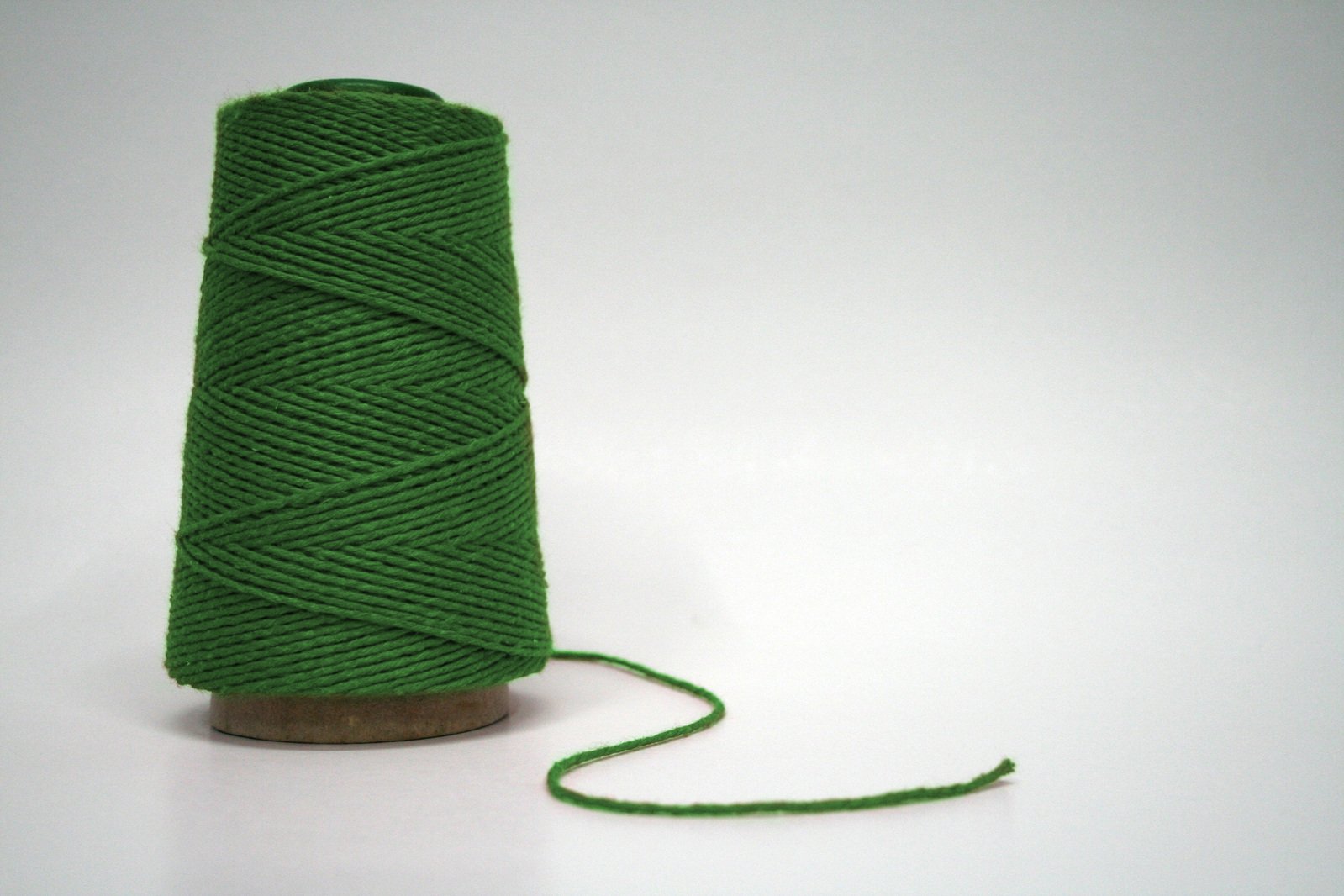 a spool of green wool next to the end of a wooden spool