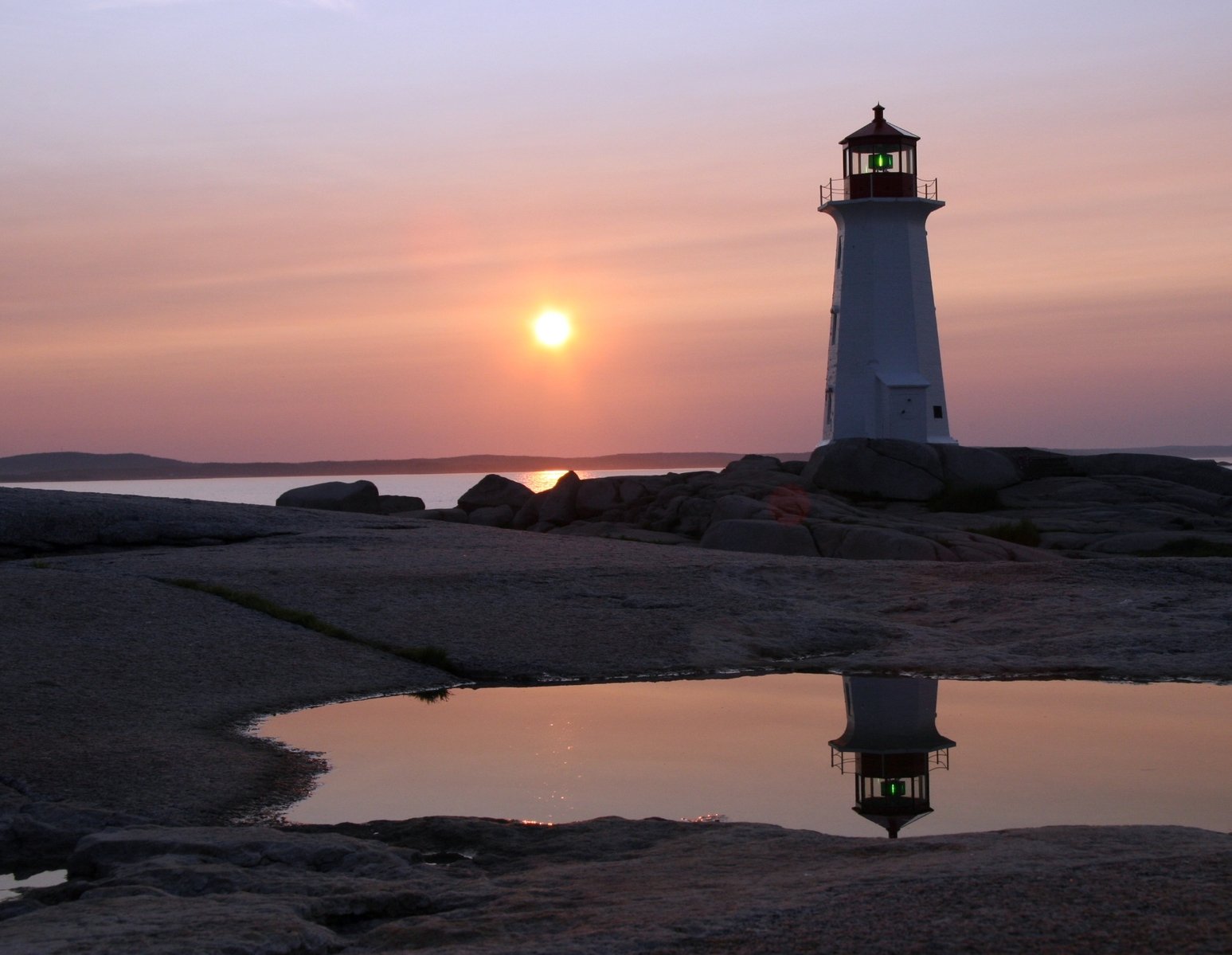 the sunset is rising over a lighthouse and rocky shoreline