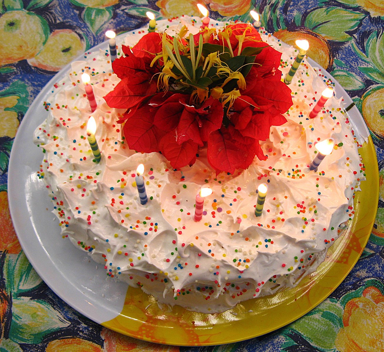 a white cake topped with a red flower and lit candles