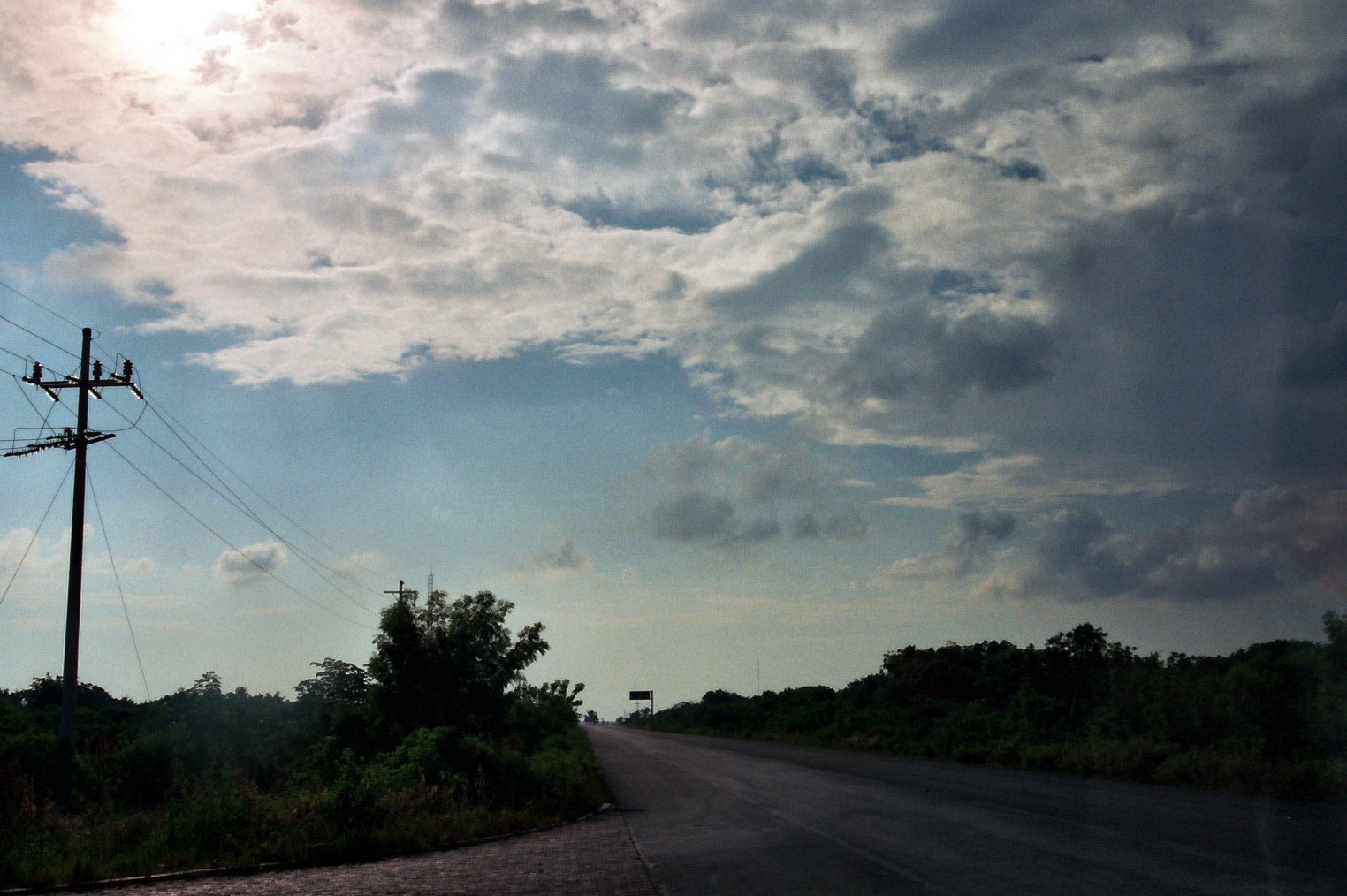 a sky filled with clouds over a rural road