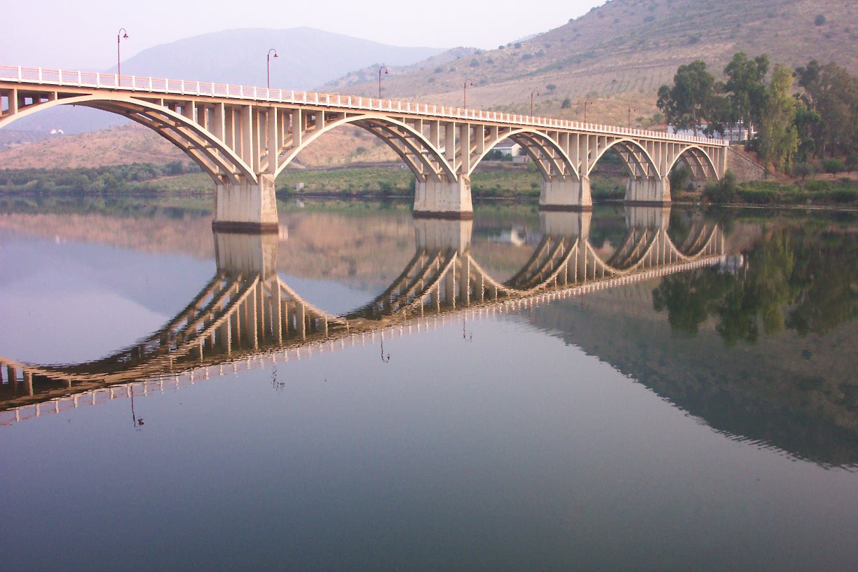 a bridge is reflected in water near a hill