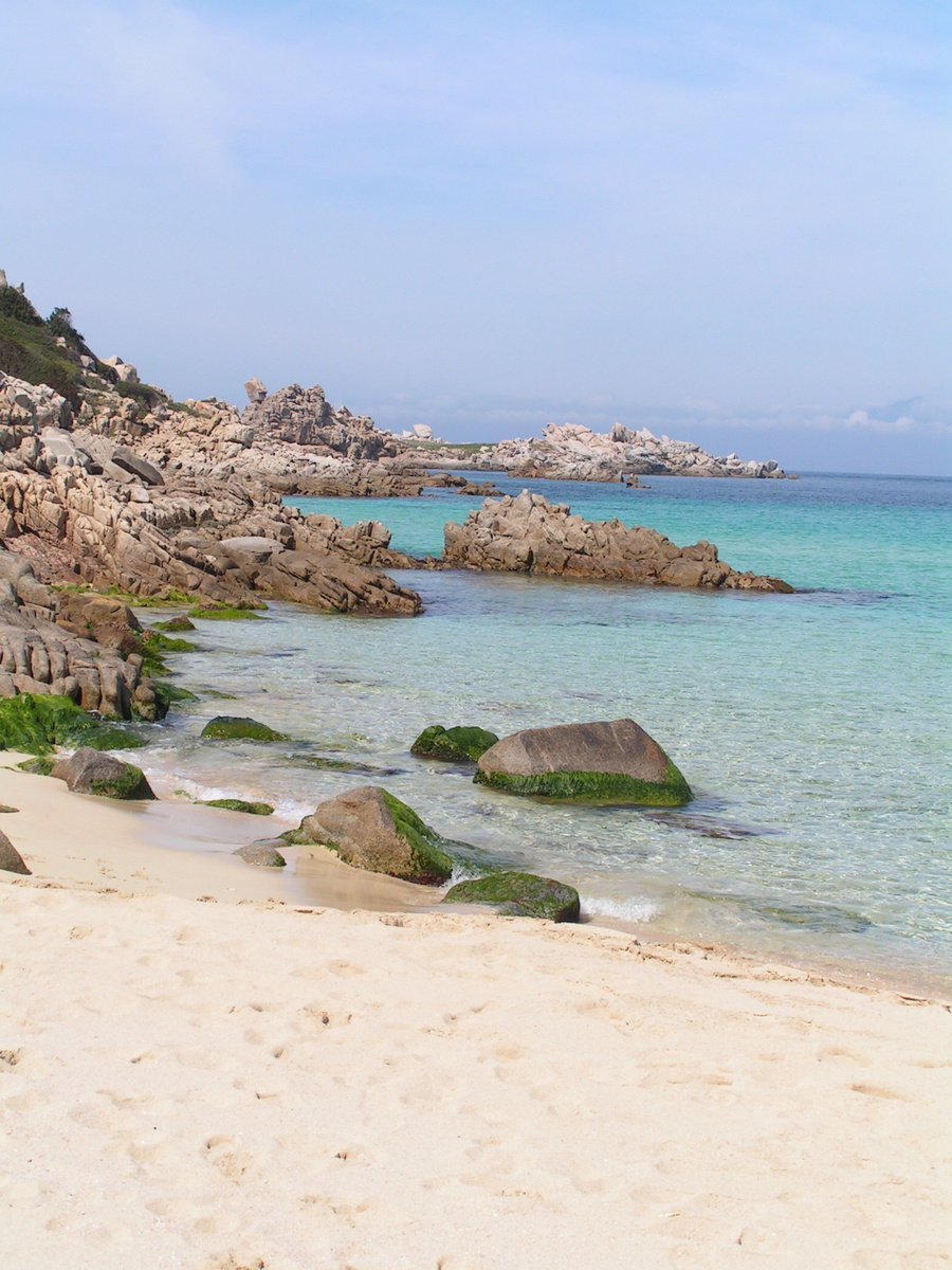 a sandy beach with several rocks in the ocean and one is empty