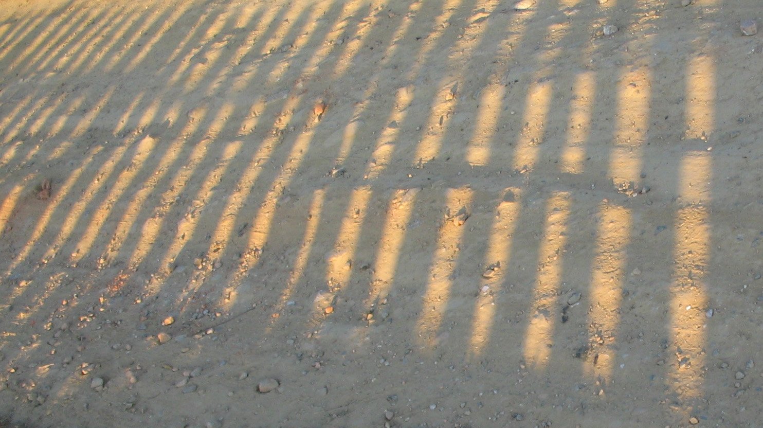 the shadow of a street sign on a dirt road